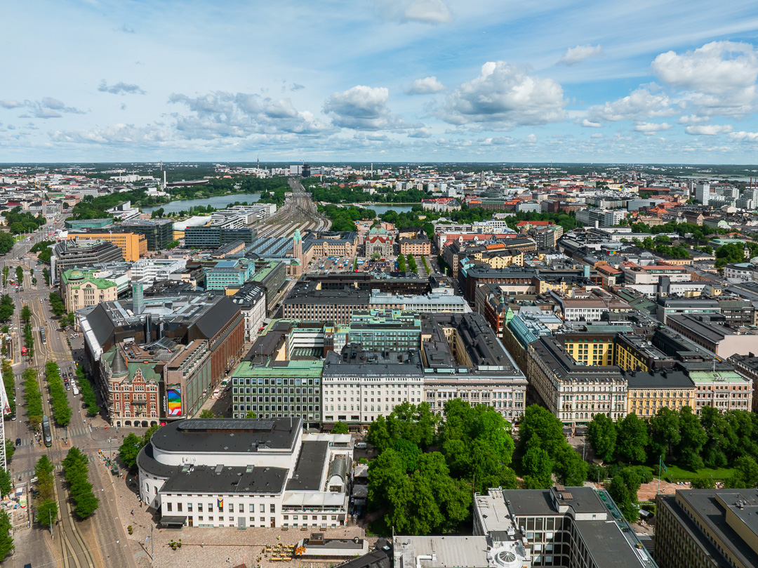 Ilmakuva kaupungista, jossa on värikkäitä rakennuksia, leveitä katuja ja vihreitä puita osittain pilvisen taivaan alla. Yhdessä rakennuksessa näkyy Pride-lippu.